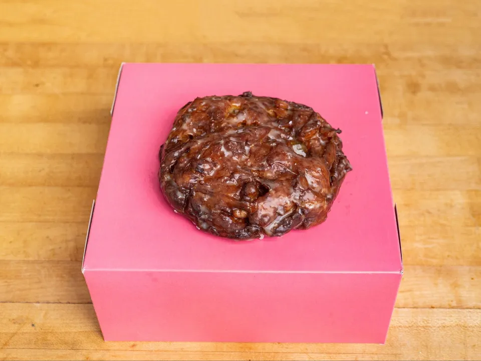 An apple fritter on a pink box.