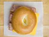 A bagel sandwich with sliced meat and cheese, on white paper.