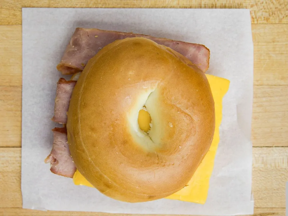 A bagel sandwich with sliced meat and cheese, on white paper.