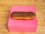 A long bar donut with chocolate glaze, on a pink box.