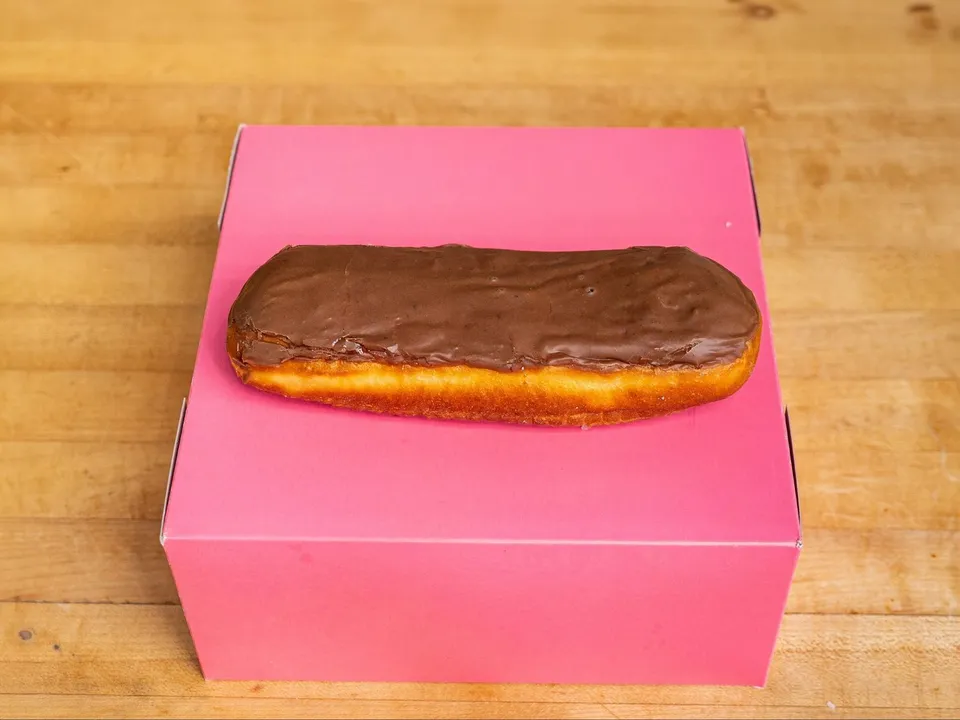 A long bar donut with chocolate glaze, on a pink box.