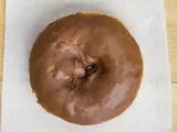 A cake donut with chocolate glaze, on white paper.