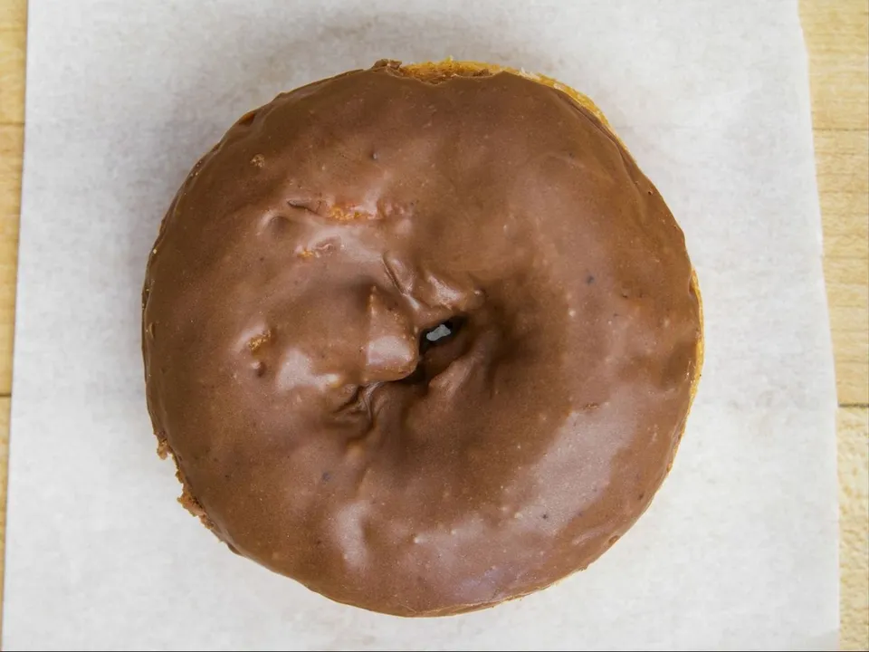 A cake donut with chocolate glaze, on white paper.