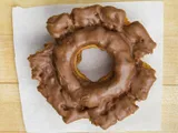 An old fashioned donut with chocolate glaze, on white paper.