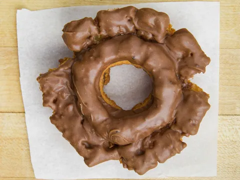 An old fashioned donut with chocolate glaze, on white paper.