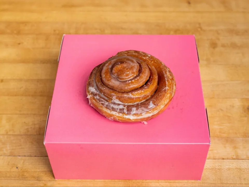 A glazed cinnamon roll on a pink box.