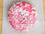 A donut with pink glaze and shredded coconut, on white paper.