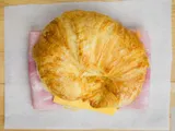 A croissant sandwich with ham and cheese, on white paper.