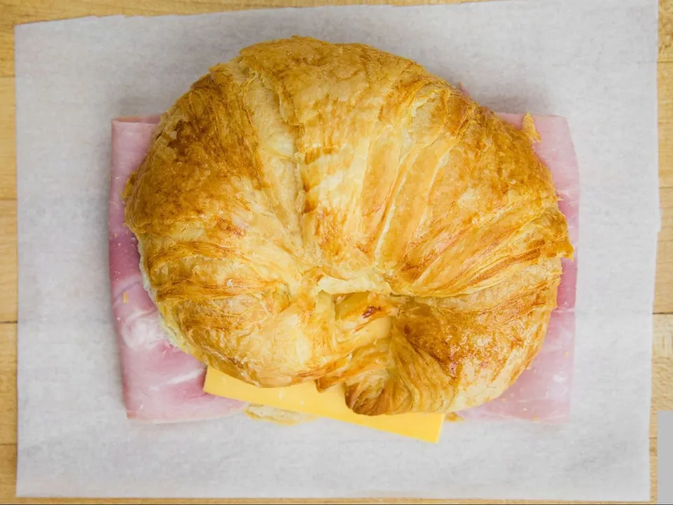 A croissant sandwich with ham and cheese, on white paper.
