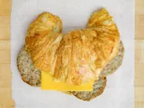 A croissant sandwich with sausage patties and cheese, on white paper.