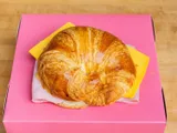 A croissant sandwich with sliced turkey and cheese, on a pink box.