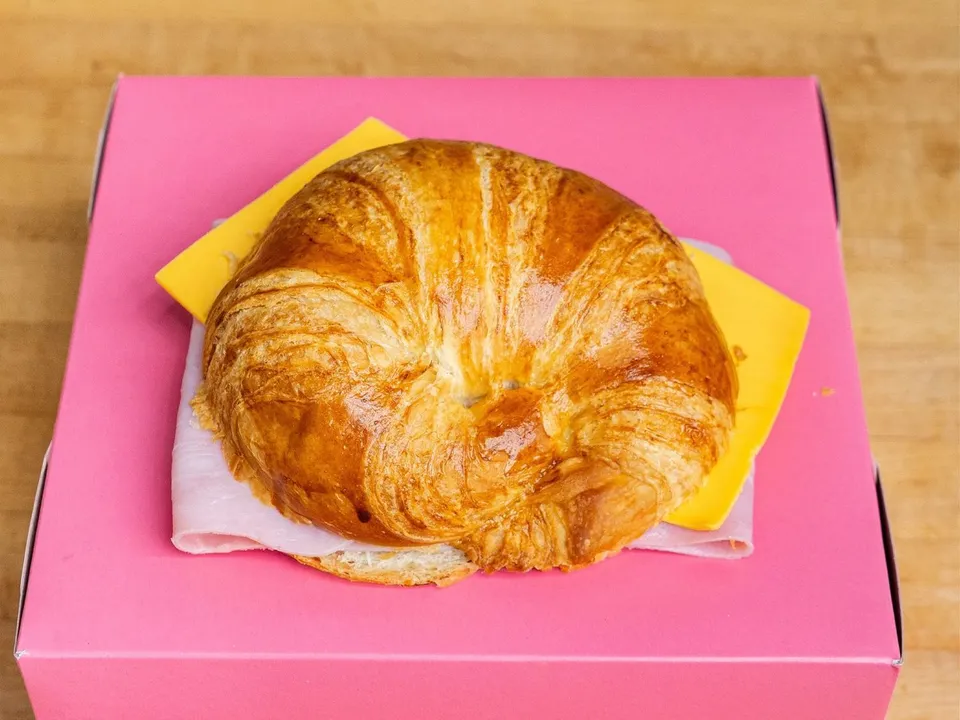 A croissant sandwich with sliced turkey and cheese, on a pink box.