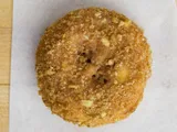 A cake donut covered in crumb topping, on white paper.