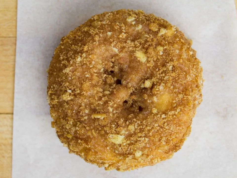 A cake donut covered in crumb topping, on white paper.