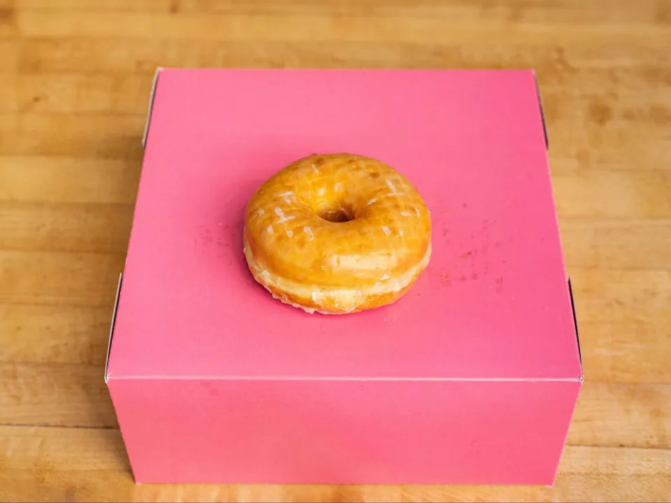 A glazed donut on a pink box.