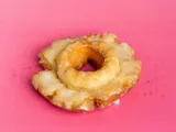 A glazed old fashioned donut on a pink background.