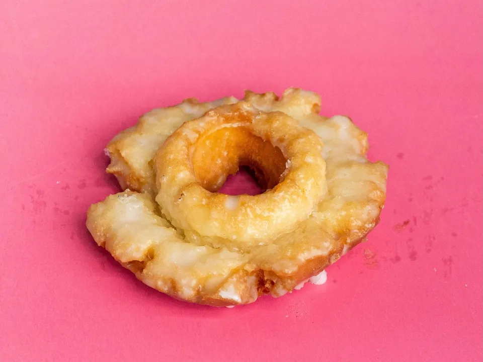 A glazed old fashioned donut on a pink background.