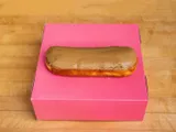 A long bar donut with maple glaze, on a pink box.