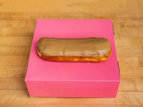 A long bar donut with maple glaze, on a pink box.