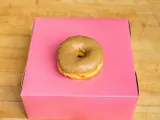 A donut with maple glaze, on a pink box.