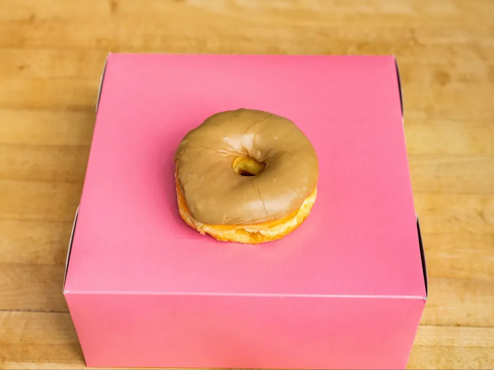 A donut with maple glaze, on a pink box.