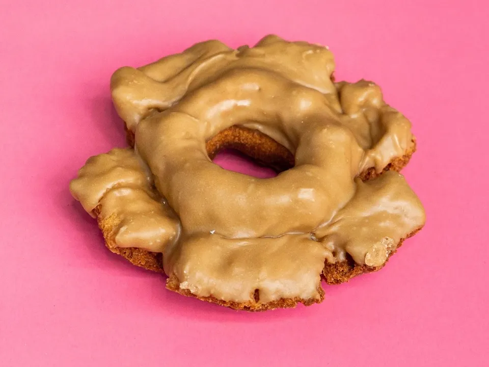 An old fashioned donut with maple glaze, on a pink background.