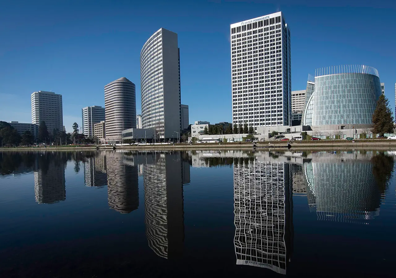 Office towers and the Cathedral of Christ the Light reflected in the still water of Lake Merritt, Oakland, under a clear blue sky.