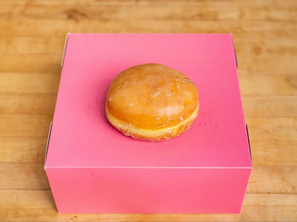 A round filled donut with glaze, on a pink box.