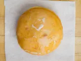 A round filled donut with glaze, on white paper.