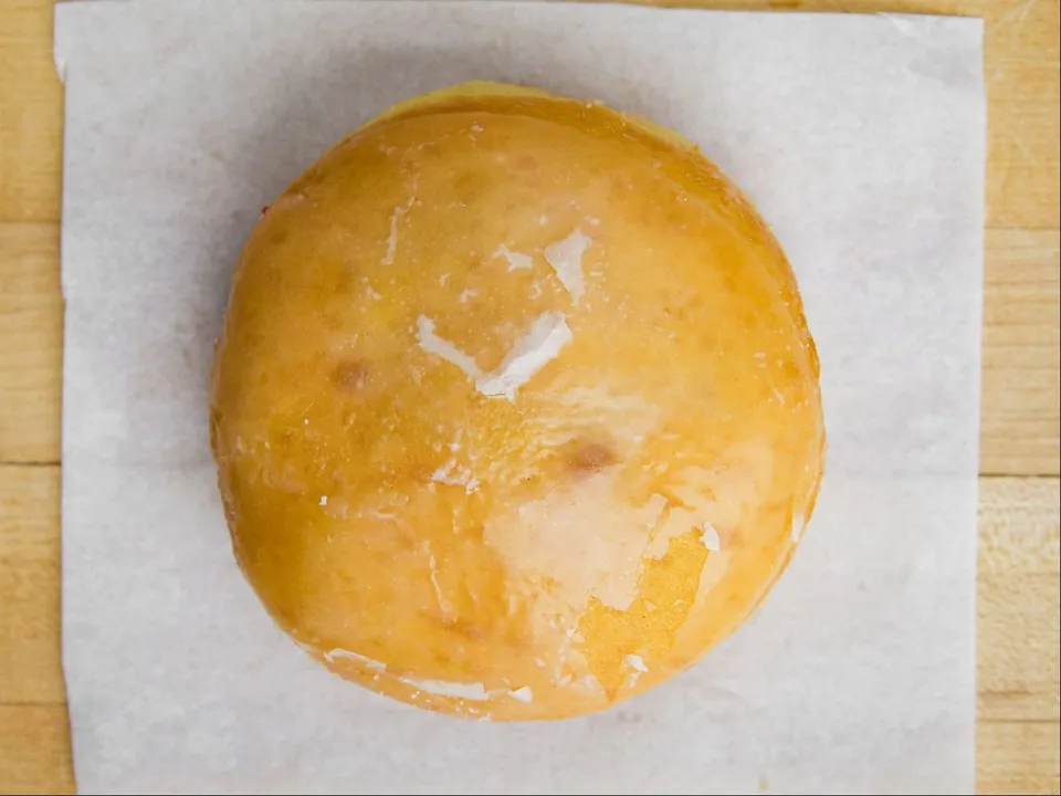 A round filled donut with glaze, on white paper.