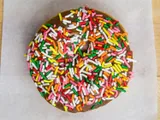 A cake donut with chocolate glaze and rainbow sprinkles, on white paper.