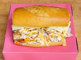 A turkey and cheese sandwich on a roll, on a pink box.