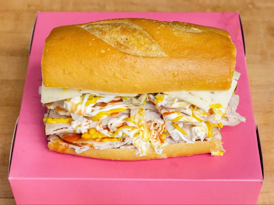 A turkey and cheese sandwich on a roll, on a pink box.